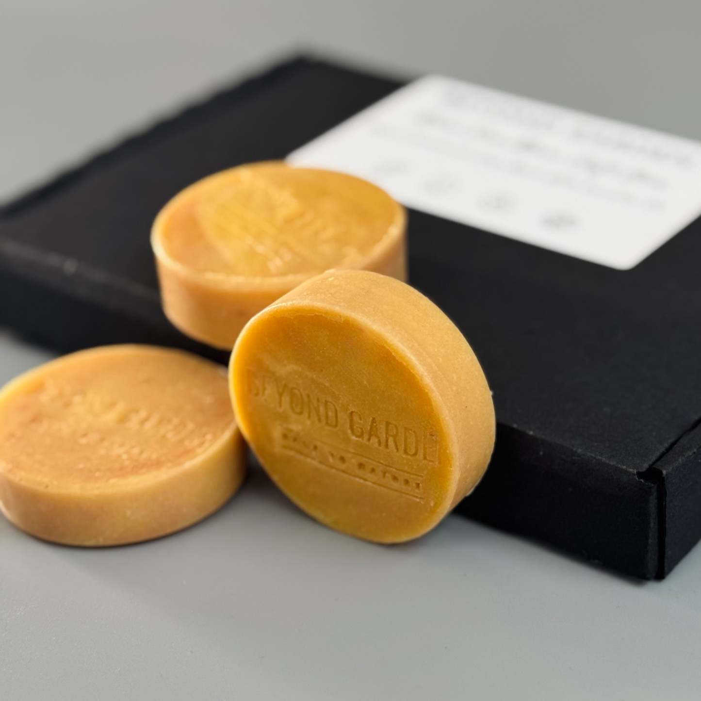 Round Irish Sea Moss guest soap resting on its side, displayed  next to a beautiful black gift box.